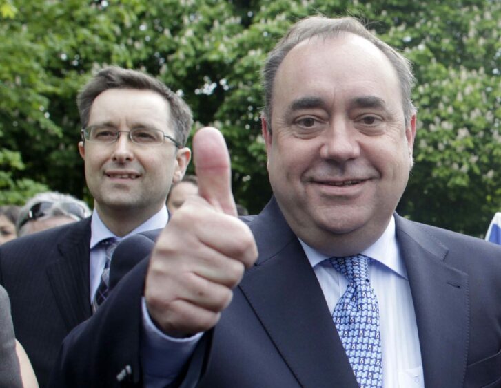 Kevin Pringle standing behind Alex Salmond, who is giving a thumbs up to the camera.