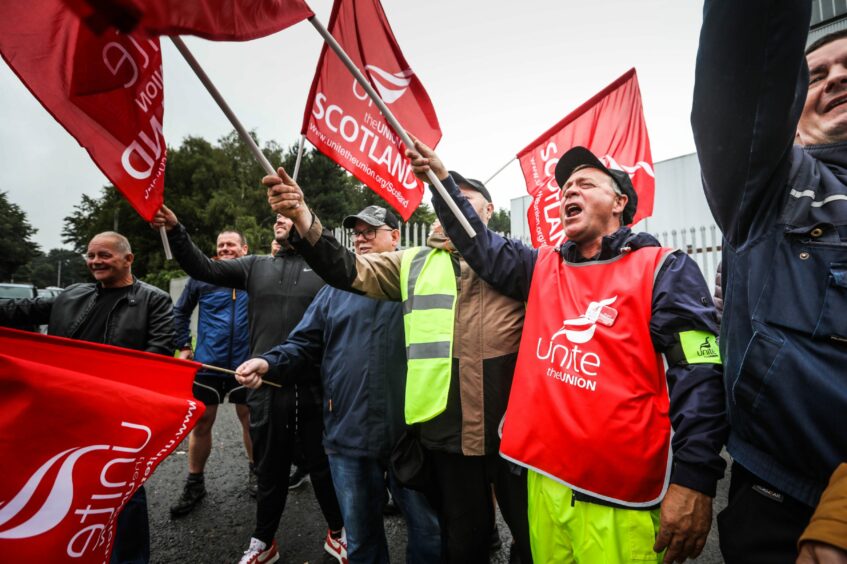 Photo shows striking refuse workers waving red 'Unite the union' banners on a picket line in Dundee.