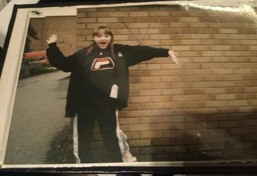 Photo shows Lynne Hoggan as a young girl, wearing a tracksuit and waving her arms.