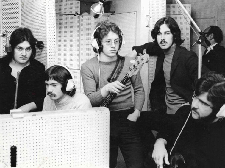 Rocker Johnny Gray shown centre of shot wearing glasses, in a recording studio with his band.