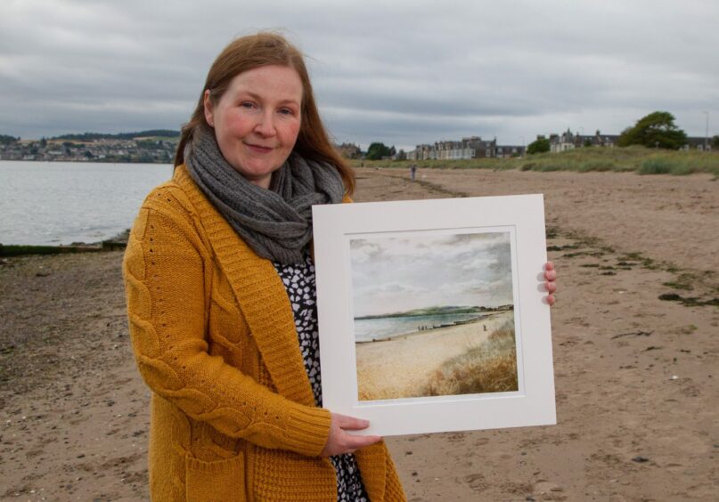 Digital artist Carol McEwan holding a painting of hers of Broughty Ferry Beach