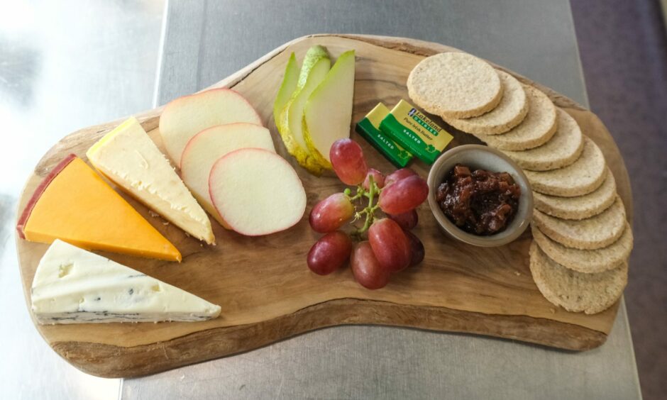 Four different cheeses, oat cakes and some grapes on a wooden charcuterie board.