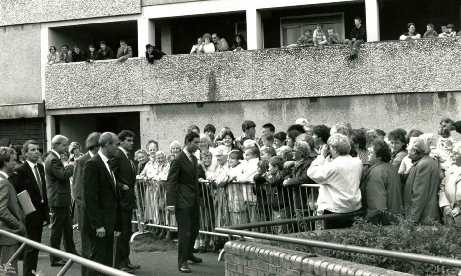Photo shows Price Charles outside a multi-storey block in Dundee, watched by large crowds.