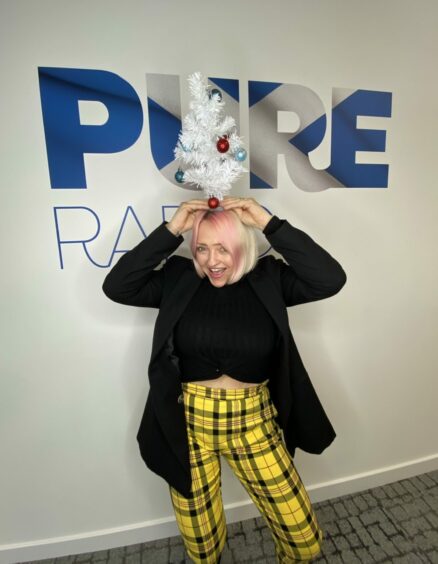 Photo shows Lynne Hoggan in front of a sign for Pure Radio.