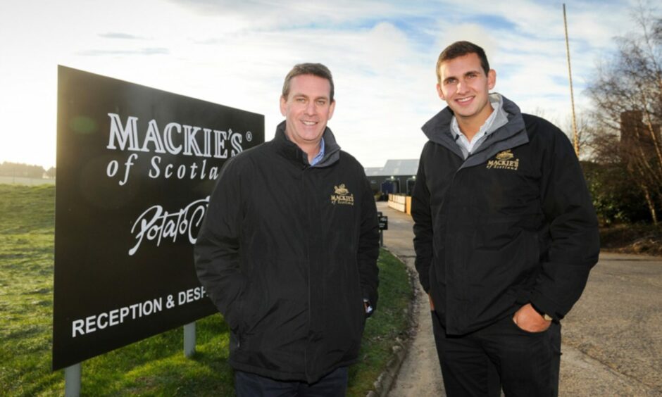 George and James Taylor standing next to Mackie's crisps sign