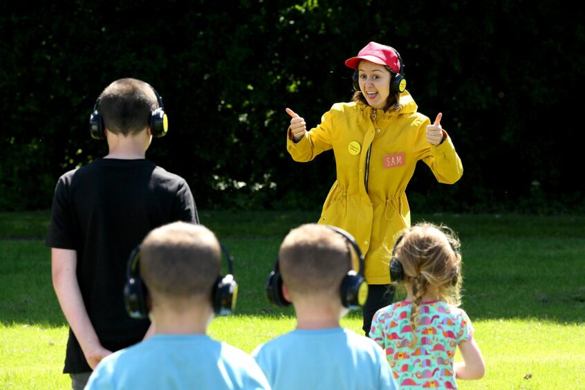 A lady in a field with children wearing headphones