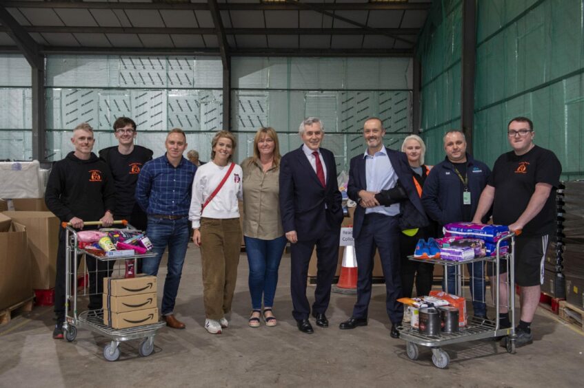 photo shows Gordon Brown with nine other people surrounded by boxes, some with Amazon labels, inside a warehouse.