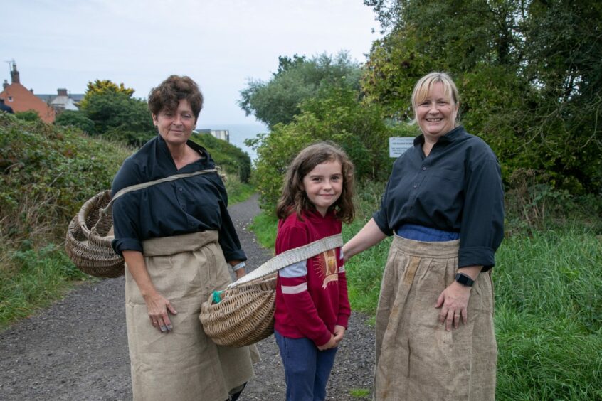 Nine-year-old Ellie Nugent learns how to carry a fish basket with Lesley Coupar and Tracy Cuthill.