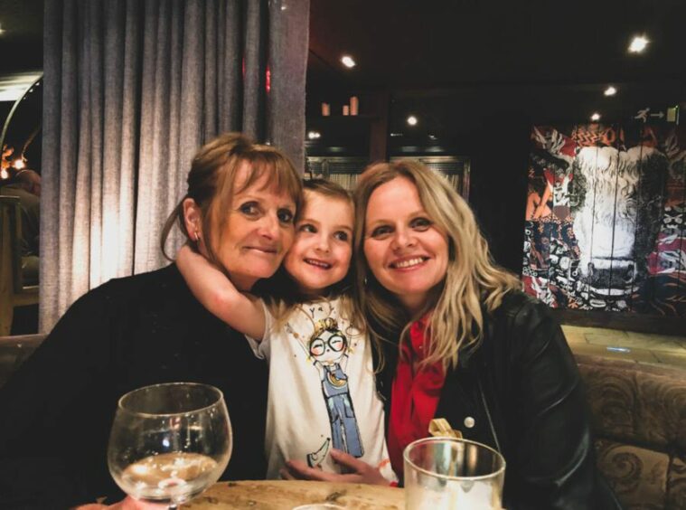 Photo shows Lindsay Bruce, sitting at a restaurant table with her mother Yvonne and in the middle, her niece Emily. All three are smiling happily.