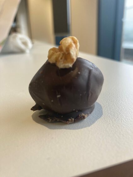 Photo shows a coffee and walnut ball, a round chocolate-covered sweet with a walnut on top.