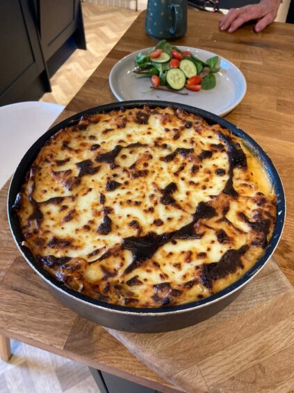 Photo shows a dish of home-made lasagne - one of the dishes in the author's family recipe book - on a kitchen table.