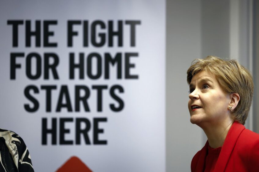 Photo shows Nicola Sturgeon in front of a large banner with the words 'the fight for home starts here' written on it.