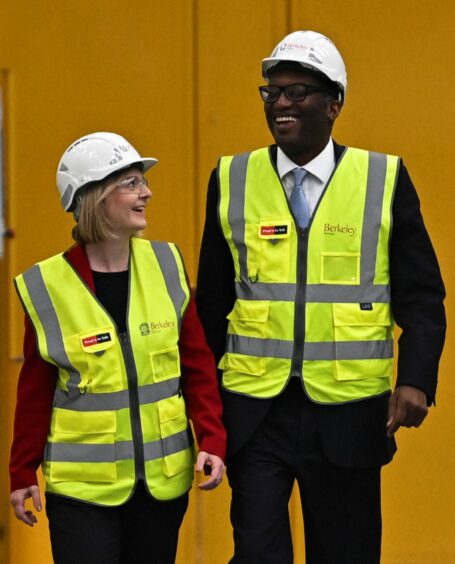 Photo shows Prime Minister Liz Truss and Chancellor of the Exchequer Kwasi Kwarteng in hard hats and hi-vis jacketrs during a photo op at an industrial site.