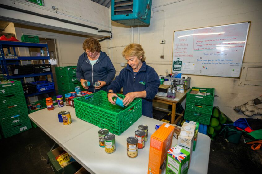 Photo shows two women volunteers packing tins and other items in a store at the Perth and Kinross Foodbank.