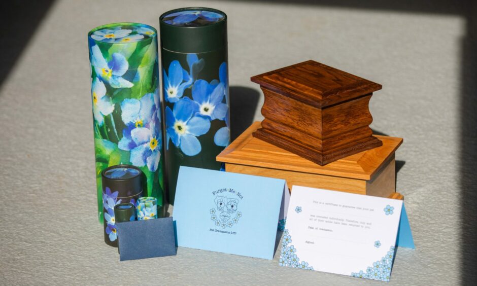 A scatter tube for pet ashes decorated with forget-me-nots and a small oak casket for pet remains.