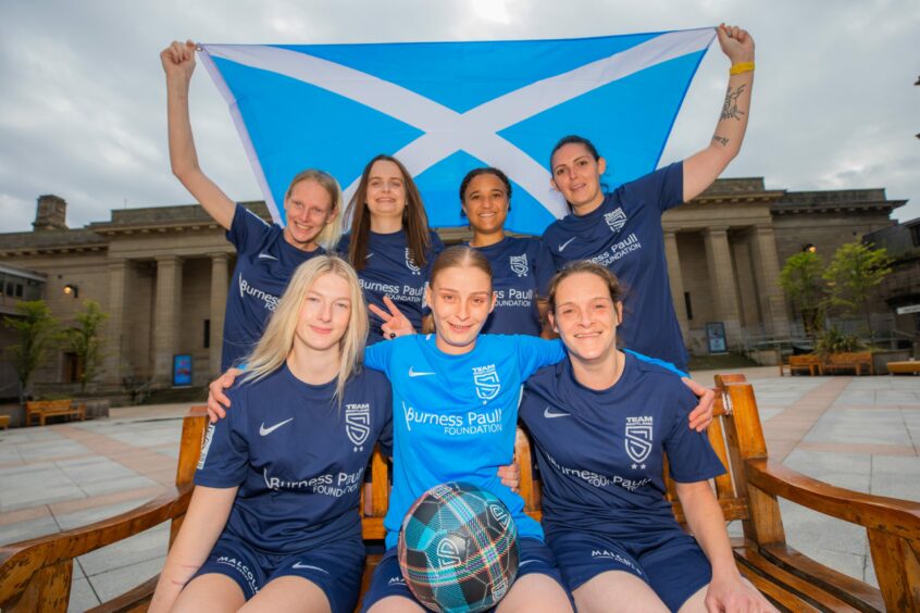 photograph shows the seven members of the Scottish women's team, holding a Scottish flag in front of the Caird Hall, Dundee.