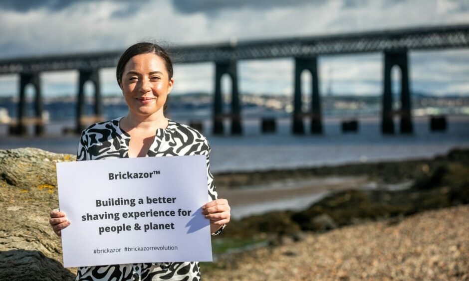 Jennifer holding a poster saying "Brickazor: Building a better shaving experience for people and planet" in front of the Tay Rail Bridge.