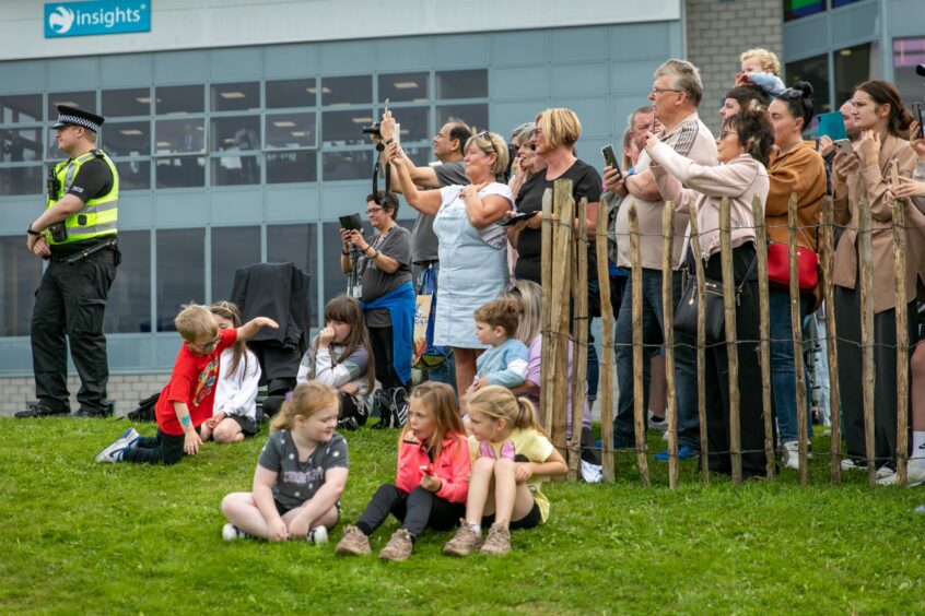 photo shows a crowd of adults and children behind a fence by the side of the A90 as the hearse carrying the Queen's coffin passes through Dundee. 
