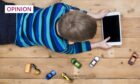 photo shows a young boy lying on a wooden floor, watching a tablet, with toy cars scattered around him.