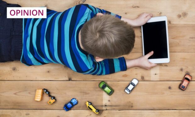 photo shows a young boy lying on a wooden floor, watching a tablet, with toy cars scattered around him.