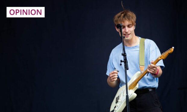photo shows the musician Sam Fender playing guitar on stage against a black background.