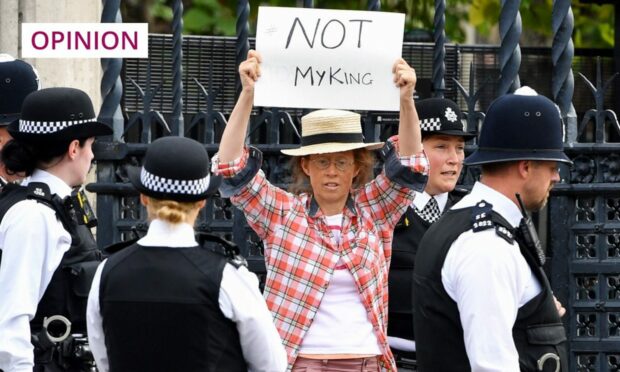 photo shows a protester holding a hand made sign which says 'Not my king', being surrounded by police officers.