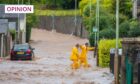 photo shows two men in yellow waterproofs, knee deep in muddy floodwater in a Perth street.