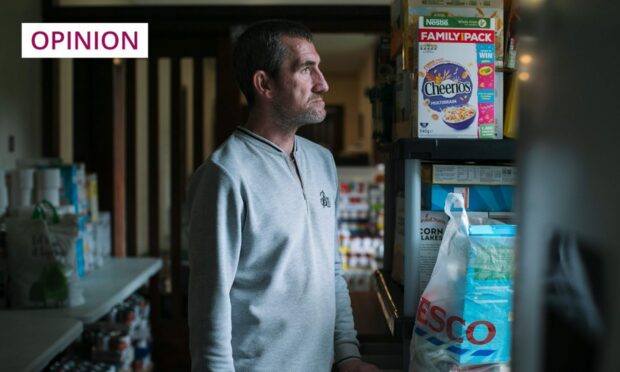 photo shows a man standing next to shelves in a foodbank.