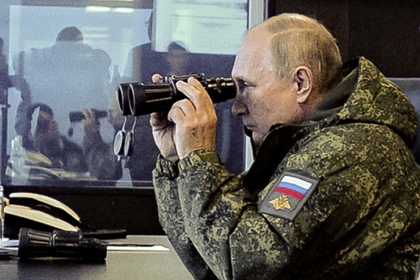 Photo shows Russian president Vladmimir Putin in military clothing, looking through binoculars.