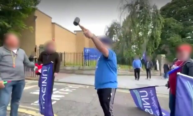 A still from the video showing the man, holding a mallet, confronting strikers at Dundee University.