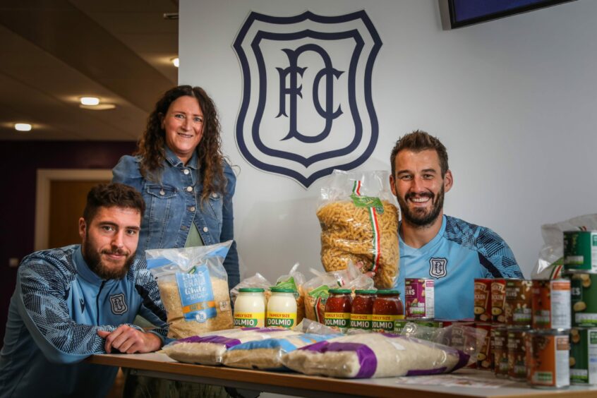 Dundee FC defender Ryan Sweeney, bookkeeper Ally Galloway and goalkeeper Adam Legzdins behind a table of foodbank donations at the club's training grounds.