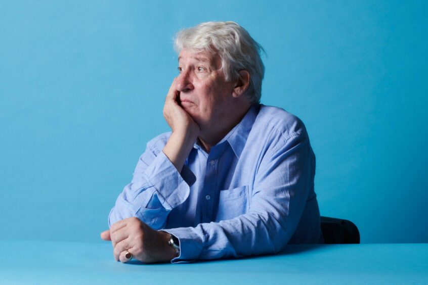 Jeremy Paxman sitting at a table and looking to the side, chin resting on his hand