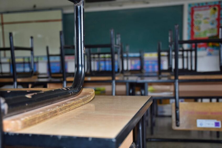Photo shows an empty school classroom, with upturned chairs on desks.