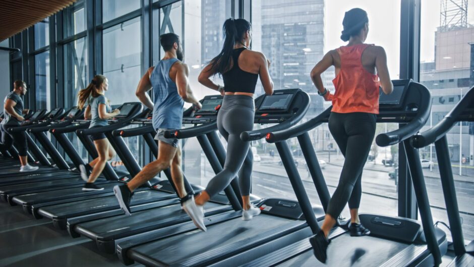 Five people running on treadmills facing a long window