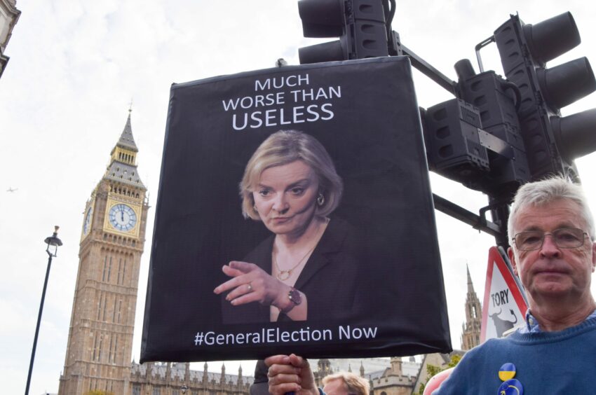 Photo shows a man with a placard featuring a photo of Liz Truss and the words 'Much worse than useless #GeneralElection now'