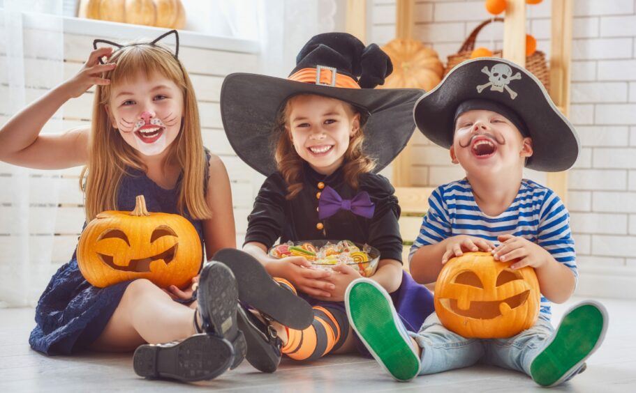 Children in halloween costumes, holding halloween carved pumpkins