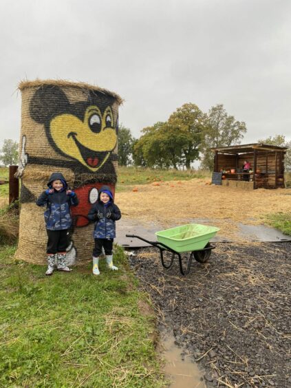 Photo shows Lynne Hoggan's two sons giving the thumbs up next to a wheelbarrow with a pumpkin patch behind them.