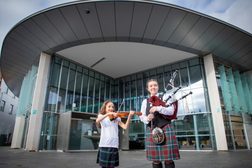 Two young girls, one with fiddle, the other bagpipes, outside Perth Concert Hall