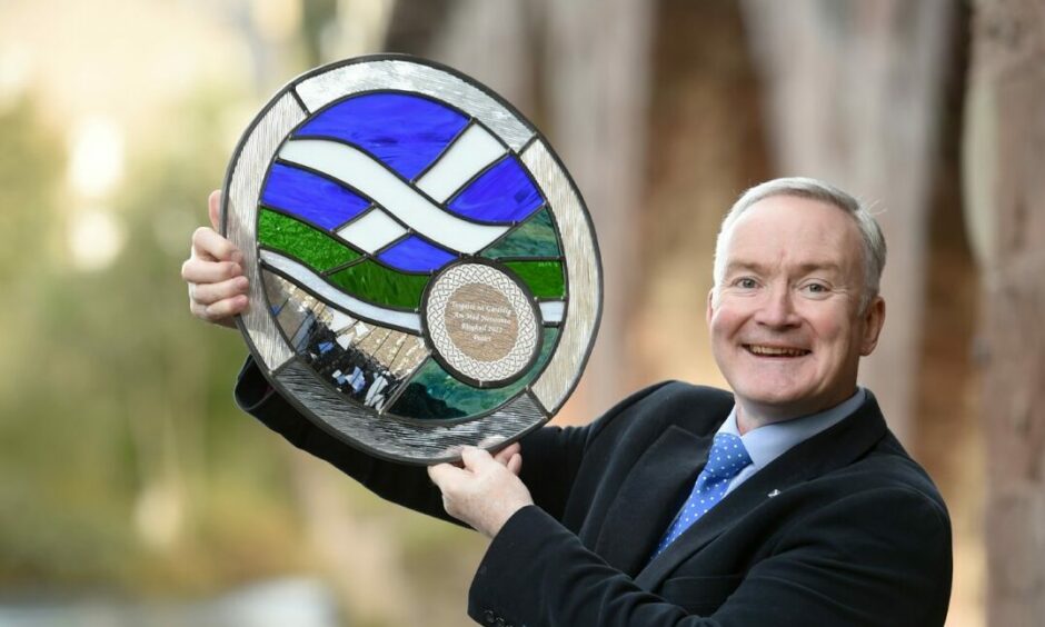 Photo shows John Urquhart holding a glass trophy awarded to him as Gaelic Ambassador of the year.