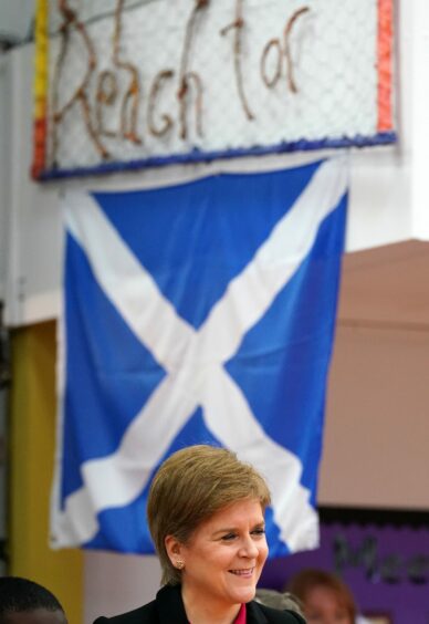 Photo shows First Minister of Scotland Nicola Sturgeon beneath a saltire flag.