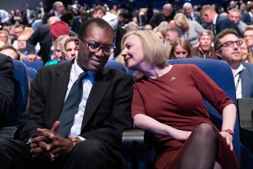 Photo shows Liz Truss and Kwasi Kwarteng speaking to one another surrounded by a large audience.
