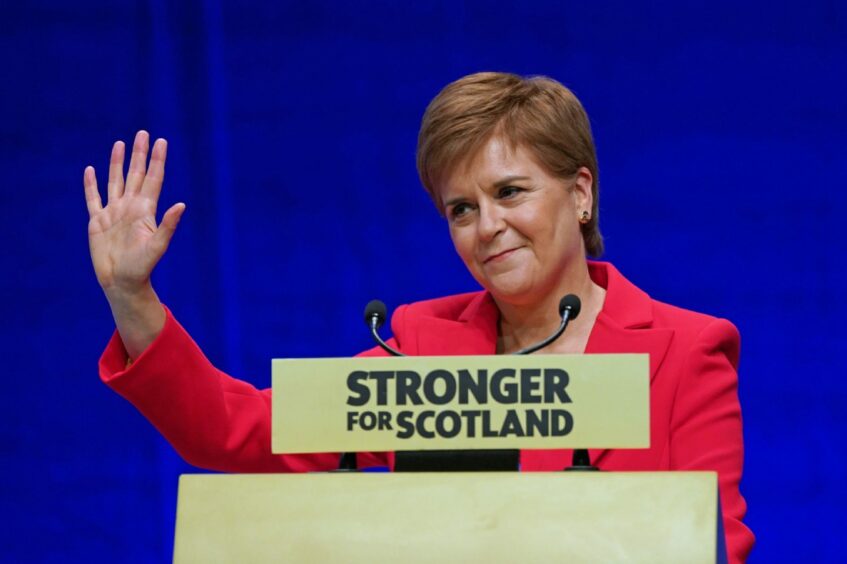 Photo shows Nicola Sturgeon waving from a podium at the SNP conference.