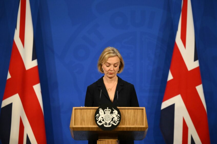 Photo shows Liz Truss looking down at the podium in the Downing Street briefing room with two Union flags behind her.