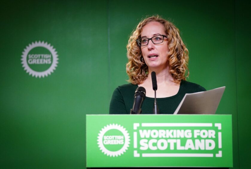 Lorma Slater at a podium with the Scottish Greens 'Working for Scotland' slogan.