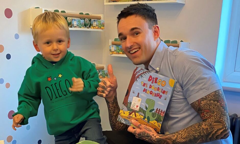 Tattoo artist Scott Mitchell holding his book, accompanied by his son, three-year-old Miles.