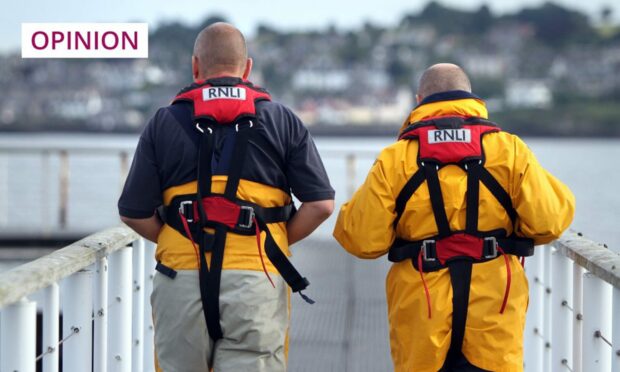 Photo shows two RNLI crewman from behind walking on the gangway to the Broughty Ferry RNLI station with the River Tay in the background.