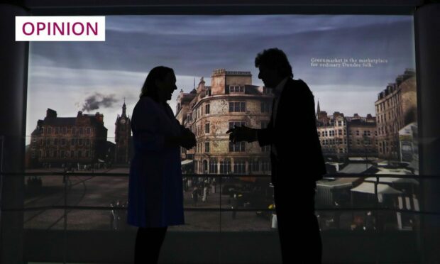 Photo shows two people standing in front of a windoe pane with an image of Dundee from decades ago.