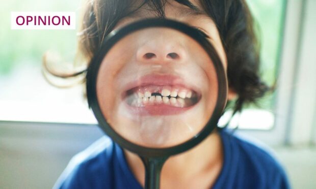 Photo shows a small boy holding a magnifying glass in front of his gap-toothed smile.