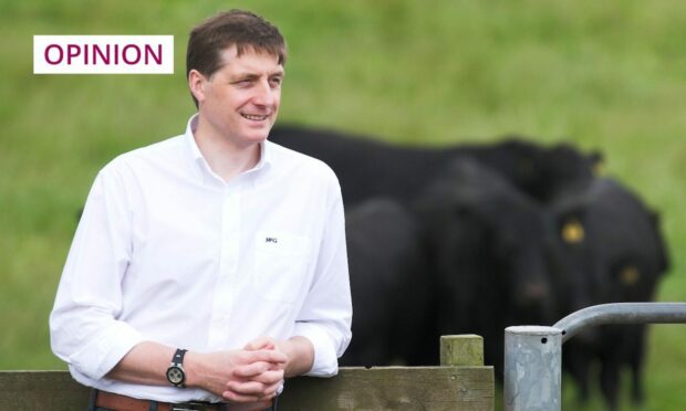Photo shows Simon Howie standing next to a field of cattle.