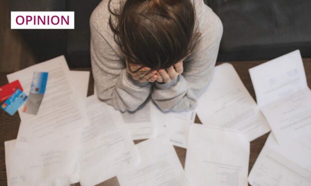 Photo shows a woman with her head in her hands and a table covered in bills and final demand letters.